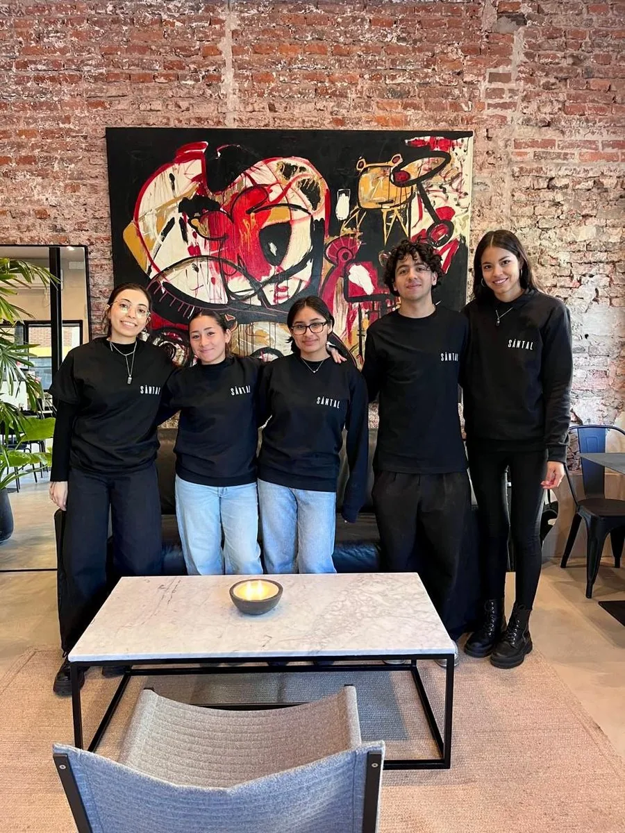 Equipo de SĀNTAL Chacarita en el salón del nuevo local de Loyola 1599 — seis personas con buzos y remeras negras con el logo SĀNTAL, frente a una pared de ladrillo expuesto y obra de arte abstracta.