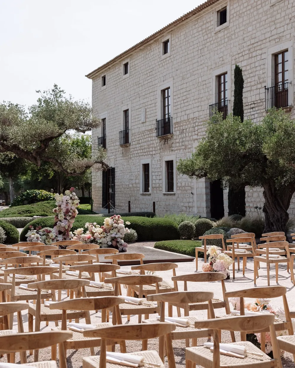 Outdoor ceremony in the gardens of Finca Morneta, with wooden chairs and floral arrangements in front of the house
