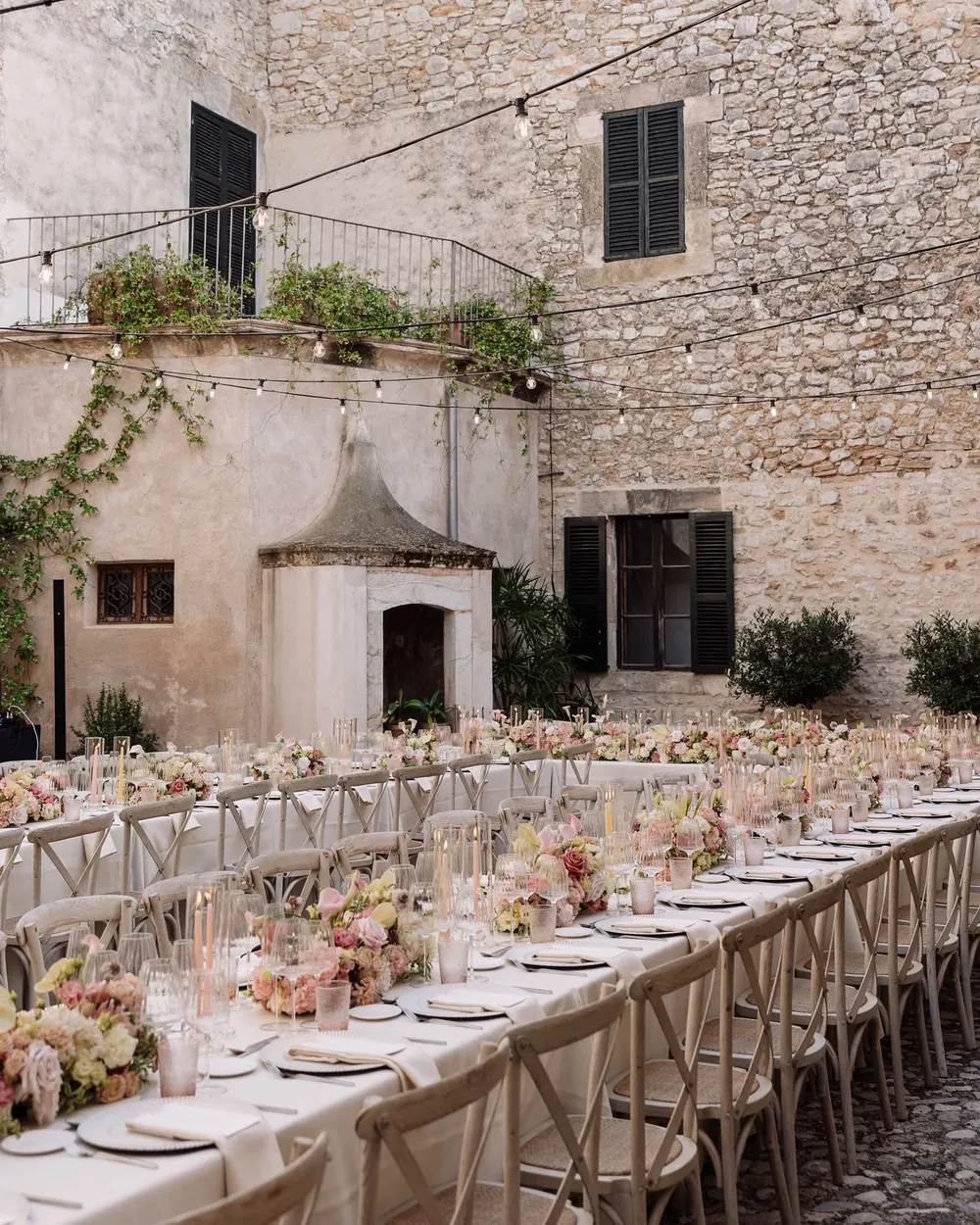 Wedding dinner in the cobbled courtyard of Finca Morneta, with long tables, pink flowers and string lights