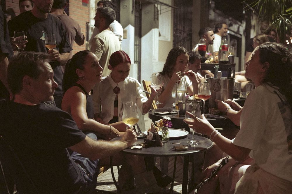 Mesas en la vereda de SĀNTAL Colegiales con copas de vino durante las Noches de Vinilos