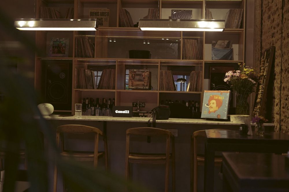 Barra de vinilos de SĀNTAL Colegiales con estantes de discos, parlantes hi-fi y cartel de Canal22