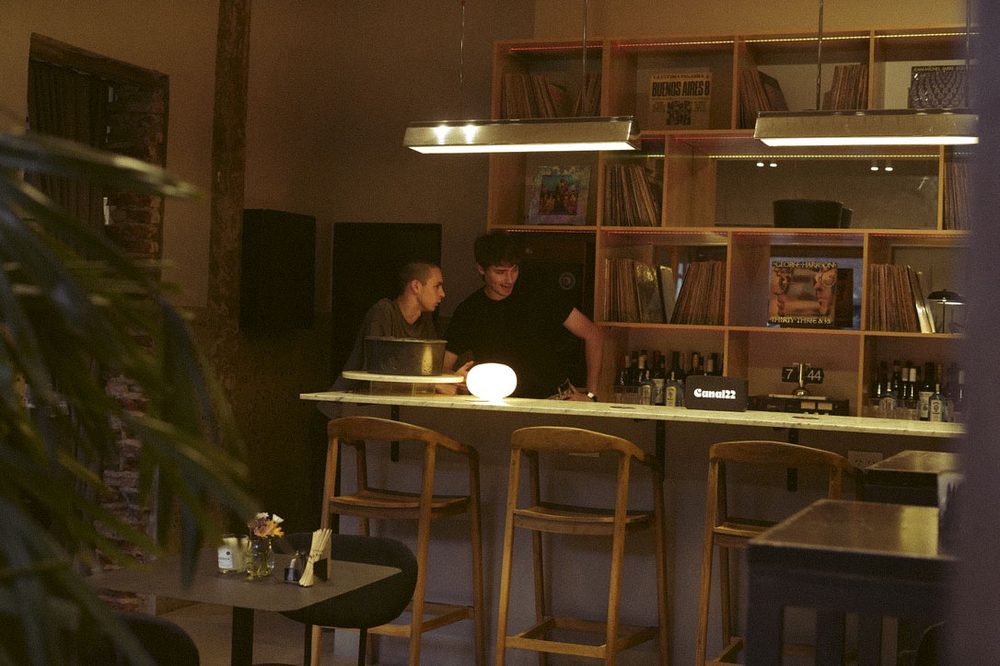 Amigos en la barra de vinilos de SĀNTAL Colegiales con lámpara cálida y estantes de discos