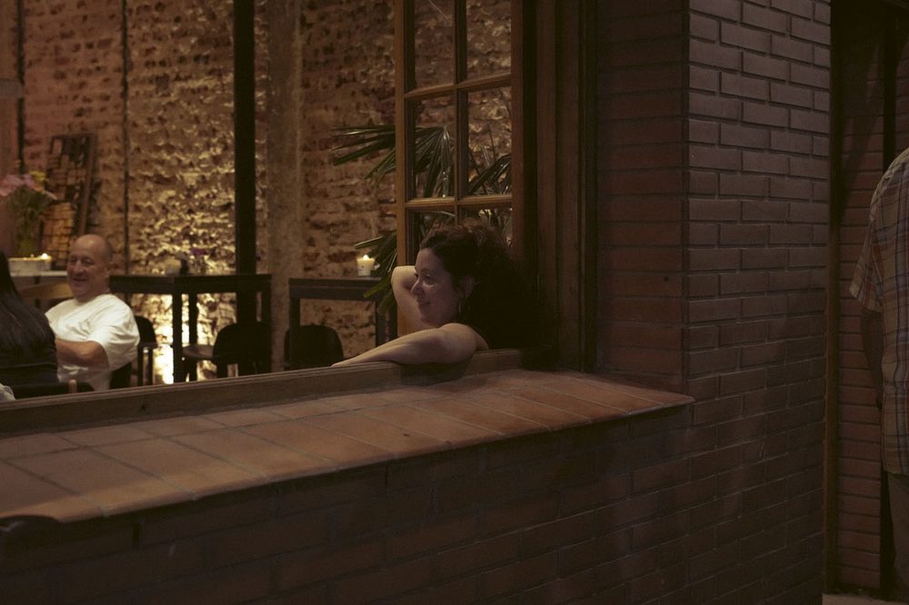 Clienta apoyada en la ventana de ladrillo del bar SĀNTAL Colegiales durante la noche de vinilos